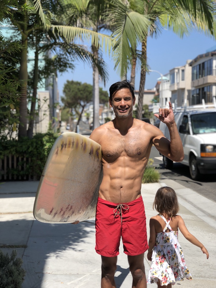 Khe holding a surfboard with a sixpack.